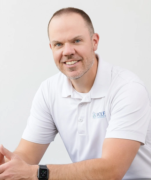 Dr. Duane Wolff wearing a white polo shirt with the Wolff Chiropractic logo